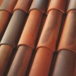 Close-up view of overlapping terracotta roof tiles in shades of reddish-brown and orange, arranged in a neat, repeating pattern.
