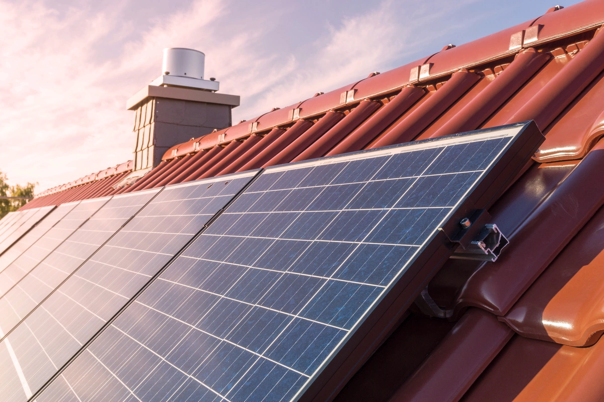 Close-up of solar panels installed on a red tiled roof, with a chimney in the background and a partly cloudy sky at sunset—highlighting how much do solar panels cost in Florida for homeowners seeking sustainable energy solutions.