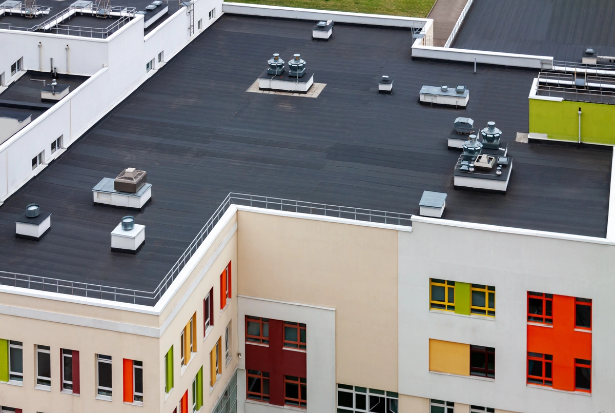 Aerial view of a modern building with a dark flat roof, multiple HVAC units, and white and beige walls featuring colorful window frames—an ideal candidate for routine commercial roof maintenance.