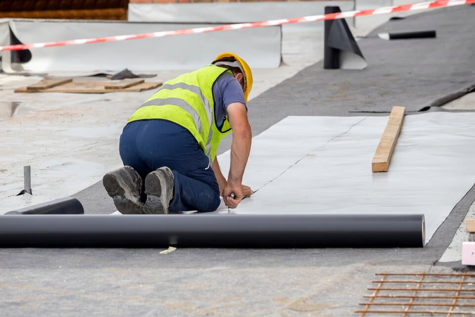 pvc roofing-roofer in safety vest and hat installing pvc roofing materials on commercial roof
