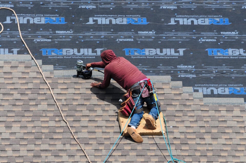 synthetic roof underlayment-roofer installing gray architectural shingles over underlayment