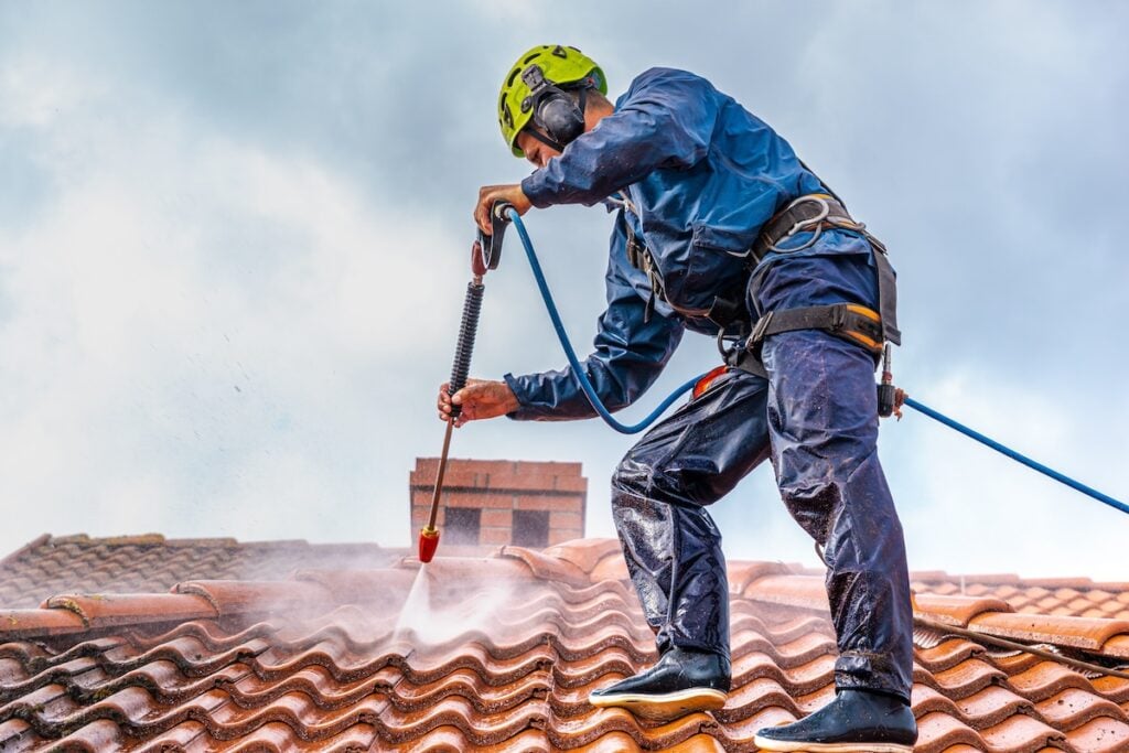 worker power washing roof