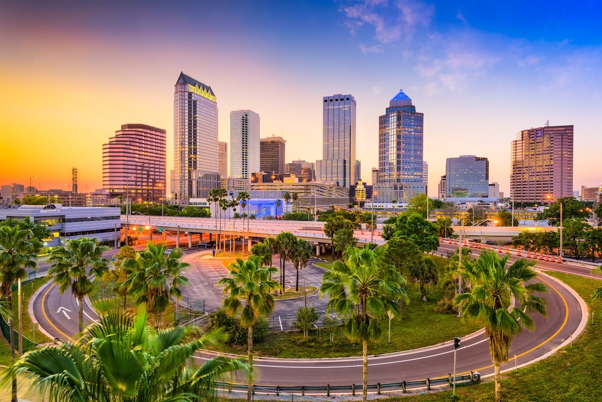Downtown Tampa, Florida skyline at sunset, featuring modern high-rise buildings home to thriving Tampa businesses, palm trees, and a roundabout road in the foreground under a colorful sky.