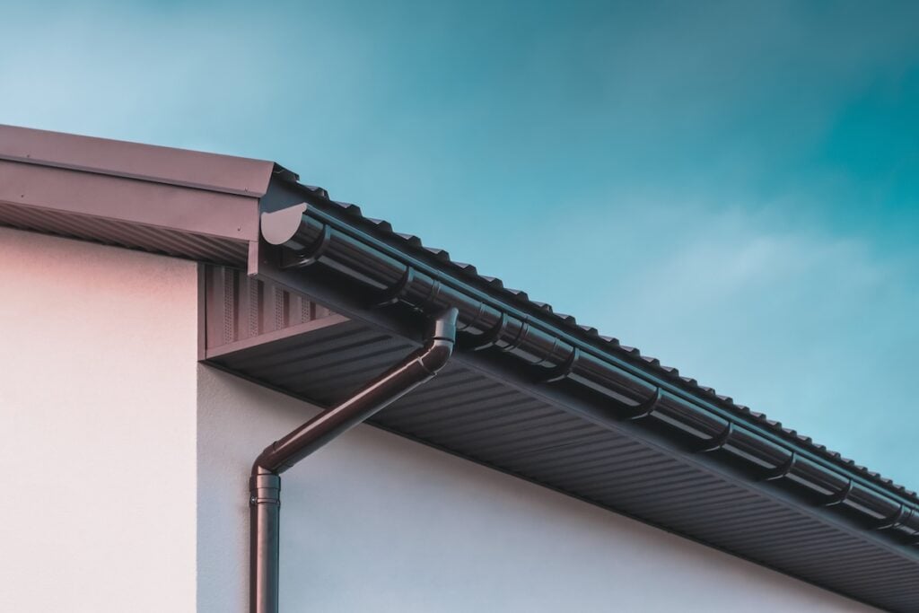 Chocolate-colored plastic gutter on the roof of the building and downpipe on the wall.