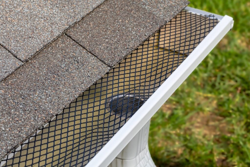 Installing gutter guard mesh screen on rain guttering. Home maintenance, yardwork and roof damage concept