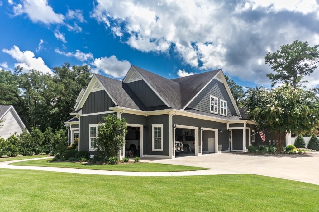 new roof financing The side view of a large gray craftsman new construction house with a landscaped yard a three car garage and driveway.
