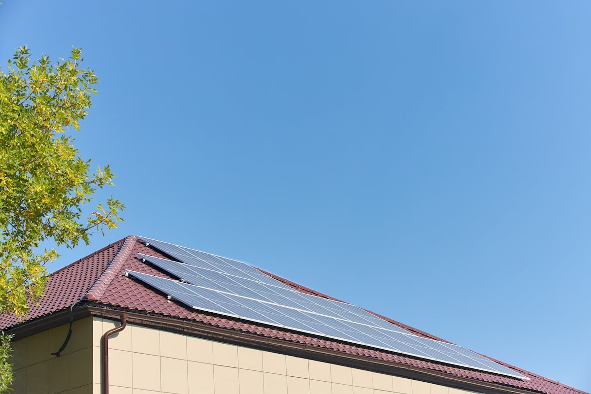 Solar panels on roof with green foliage tree and copyspace. Building with lots of solar panels. Renewable solar energy. Alternative Generator Energy efficient house uses solar energy of sun